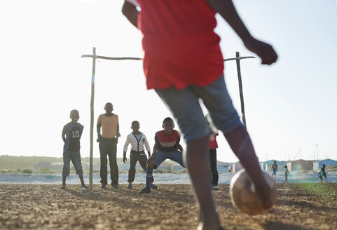 Jungen spielen zusammen Fußball auf einem unbefestigten Feld - CAIF04037
