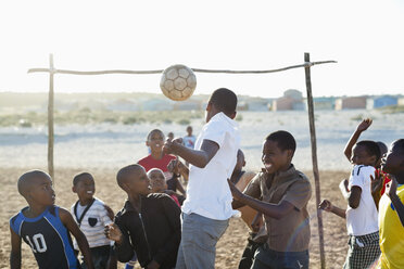 Jungen spielen zusammen Fußball auf einem unbefestigten Feld - CAIF04040