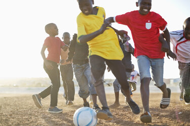 Jungen spielen zusammen Fußball auf einem unbefestigten Feld - CAIF04041