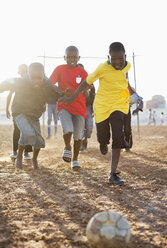 Boys playing soccer together in dirt field - CAIF04043