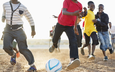 Jungen spielen zusammen Fußball auf einem unbefestigten Feld - CAIF04045