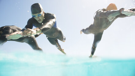 Triathletes in wetsuits running into ocean - CAIF04050