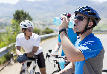 Radfahrer trinkt Wasser auf Landstraße - CAIF04054