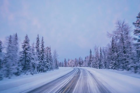 Abgelegene Winterstraße durch schneebedeckte Waldbäume vor blauem Himmel, Lappland, Finnland, lizenzfreies Stockfoto