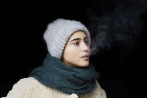 Porträt einer jungen Frau in Winterkleidung beim Rauchen, lizenzfreies Stockfoto