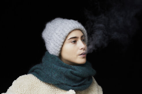 Porträt einer jungen Frau in Winterkleidung beim Rauchen - FMKF04896