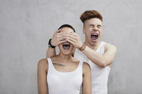 Portrait of screaming young couple wearing vests - FMKF04899