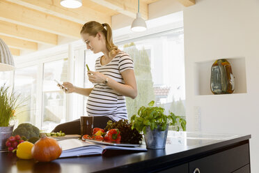 Pregnant woman in kitchen at home using cell phone - BMOF00011