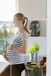 Lächelnde schwangere Frau steht in der Küche zu Hause - BMOF00012