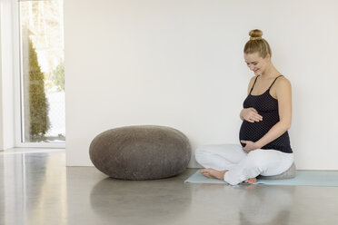 Lächelnde schwangere Frau auf einer Yogamatte sitzend - BMOF00014