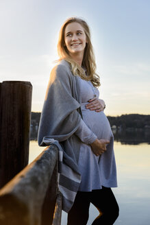 Lächelnde schwangere Frau am Seeufer stehend - BMOF00022
