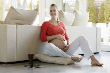 Portrait of smiling pregnant woman sitting on floor at home - BMOF00031