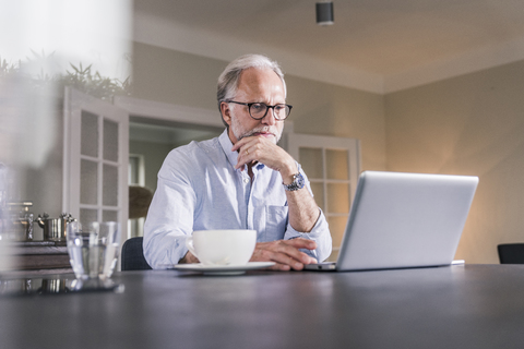 Porträt eines reifen Mannes, der zu Hause am Tisch sitzt und einen Laptop benutzt, lizenzfreies Stockfoto