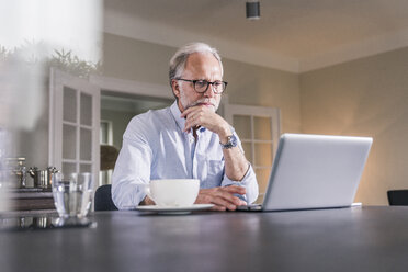 Portrait of mature man sitting at table using laptop at home - UUF12921