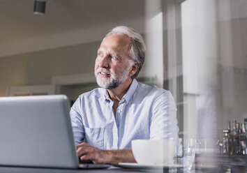 Portrait of mature man sitting at table using laptop at home - UUF12926