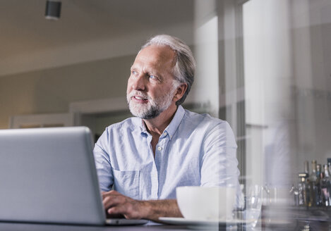 Porträt eines reifen Mannes, der zu Hause am Tisch sitzt und einen Laptop benutzt - UUF12926
