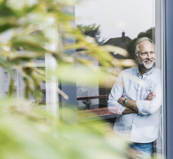 Smiling mature man looking out of terrace door - UUF12941