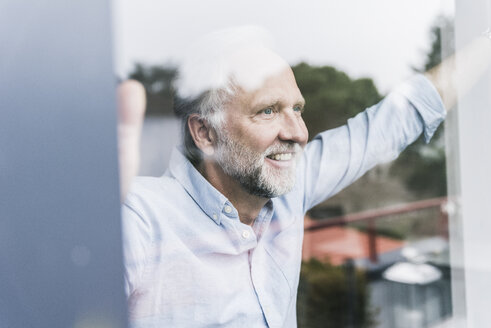 Portrait of happy mature man looking out of windowpane - UUF12942