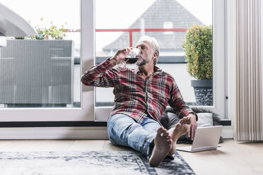 Barfuß Mann entspannt auf dem Boden zu Hause trinken Glas Rotwein - UUF12954