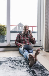 Barfuß Mann am Telefon entspannt auf dem Boden zu Hause mit Laptop und Glas Rotwein - UUF12955