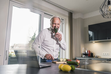 Lustiger reifer Mann isst rohe Cougette in der Küche - UUF12965