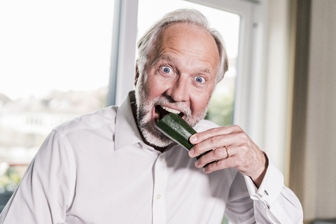 Porträt eines reifen Mannes, der in eine Zucchini beißt, lizenzfreies Stockfoto