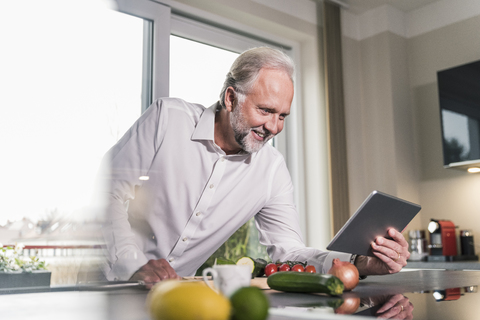 Smiling mature man using tablet in the kitchen stock photo