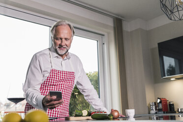 Portrait of mature man in the kitchen using cell phone - UUF12972