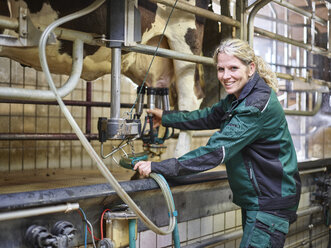 Porträt einer lächelnden Bäuerin im Stall beim Melken einer Kuh - CVF00249
