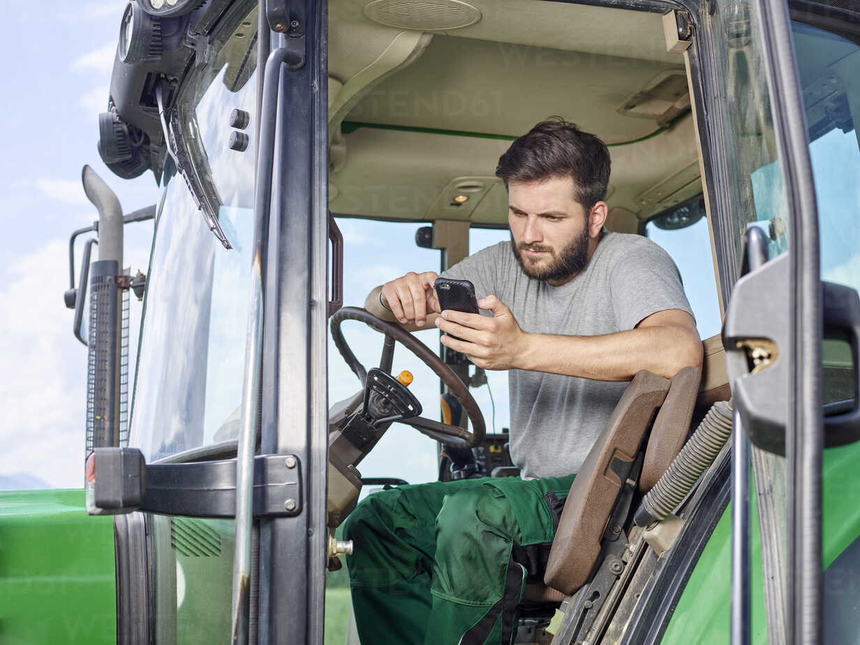 Farmer sitting on tractor using cell phone stock photo