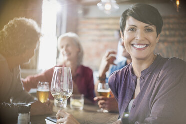 Porträt einer lächelnden Frau, die Weißwein trinkt und mit Freunden an einem Restauranttisch speist - HOXF00008