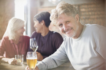 Porträt eines lächelnden älteren Mannes, der mit Freunden an einem Restauranttisch Bier trinkt - HOXF00010