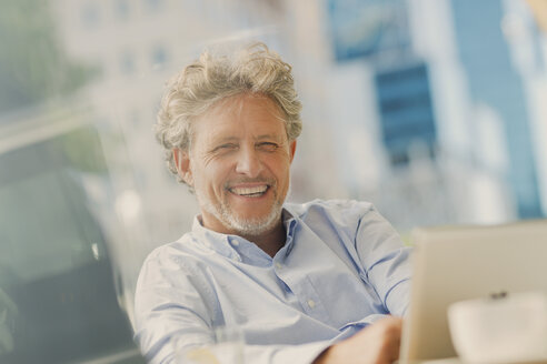 Porträt eines lächelnden Geschäftsmanns, der ein digitales Tablet in einem Straßencafé benutzt - HOXF00024