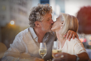 Affectionate senior couple kissing drinking white wine at sidewalk cafe - HOXF00027