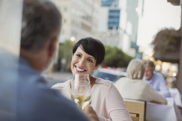 Smiling couple toasting white wine glasses at urban sidewalk cafe - HOXF00041