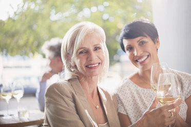 Portrait lächelnde Mutter und Tochter stoßen mit Weißweingläsern in einem sonnigen Restaurant an - HOXF00043