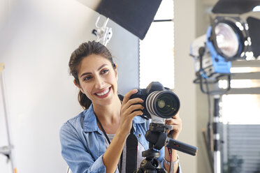 Lächelnde Fotografin hinter der Kamera im Studio - HOXF00048