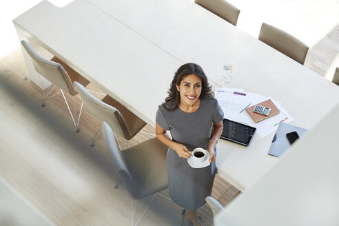 Porträt einer lächelnden Geschäftsfrau, die in einem Konferenzraum Kaffee trinkt - HOXF00057