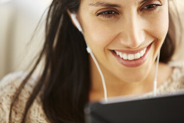 Nahaufnahme einer lächelnden Frau, die ein digitales Tablet mit Kopfhörern benutzt - HOXF00059
