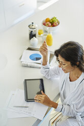 Frau im Bademantel arbeitet an einem digitalen Tablet an der Küchentheke - HOXF00065