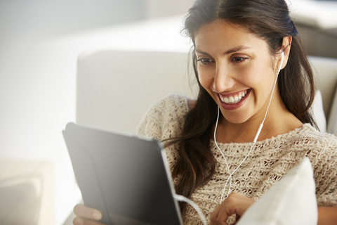 Lächelnde Frau, die ein digitales Tablet mit Kopfhörern auf dem Sofa benutzt, lizenzfreies Stockfoto