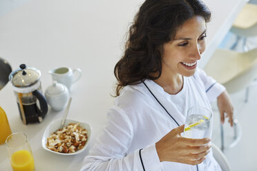Lächelnde Frau im Bademantel trinkt Wasser in der Morgenküche - HOXF00094
