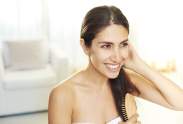 Smiling brunette woman brushing hair - HOXF00101