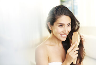 Smiling brunette woman brushing hair - HOXF00105