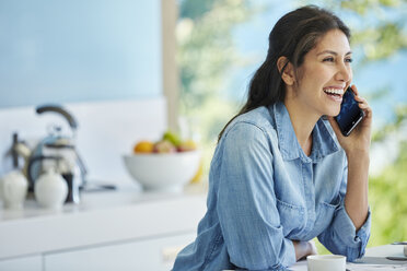 Smiling woman talking on cell phone in kitchen - HOXF00121