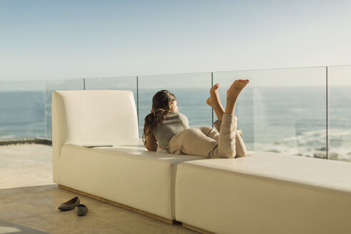 Frau auf luxuriösem Balkon entspannt auf einer Bank liegend mit Blick auf das sonnige Meer - HOXF00137