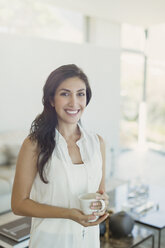 Portrait lächelnde brünette Frau trinkt Kaffee im Wohnzimmer - HOXF00144