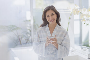 Portrait smiling brunette woman in bathrobe drinking water - HOXF00148