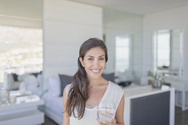 Portrait smiling brunette woman drinking water in bedroom - HOXF00155