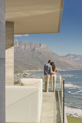 Couple looking at sunny ocean and mountain view from luxury balcony - HOXF00159